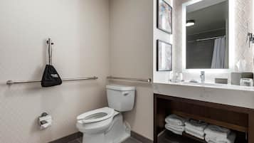 A bathroom with a toilet, handrails, a towel rack, a sink, and a mirror.