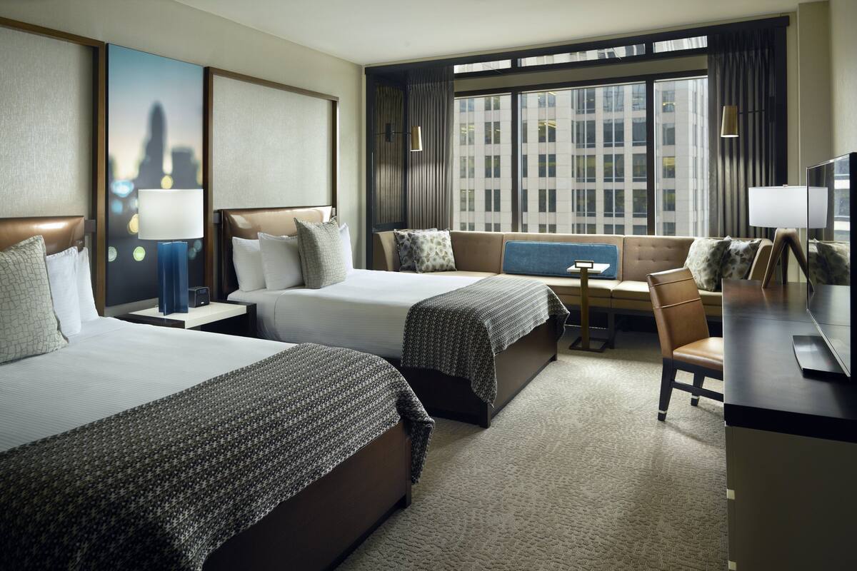 A hotel room with two beds, a sofa, a desk, and a TV.