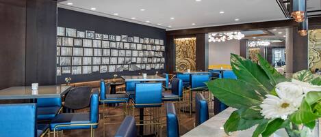 A modern restaurant with blue upholstered chairs and tables, a marble counter, and a wall decorated with framed pictures.