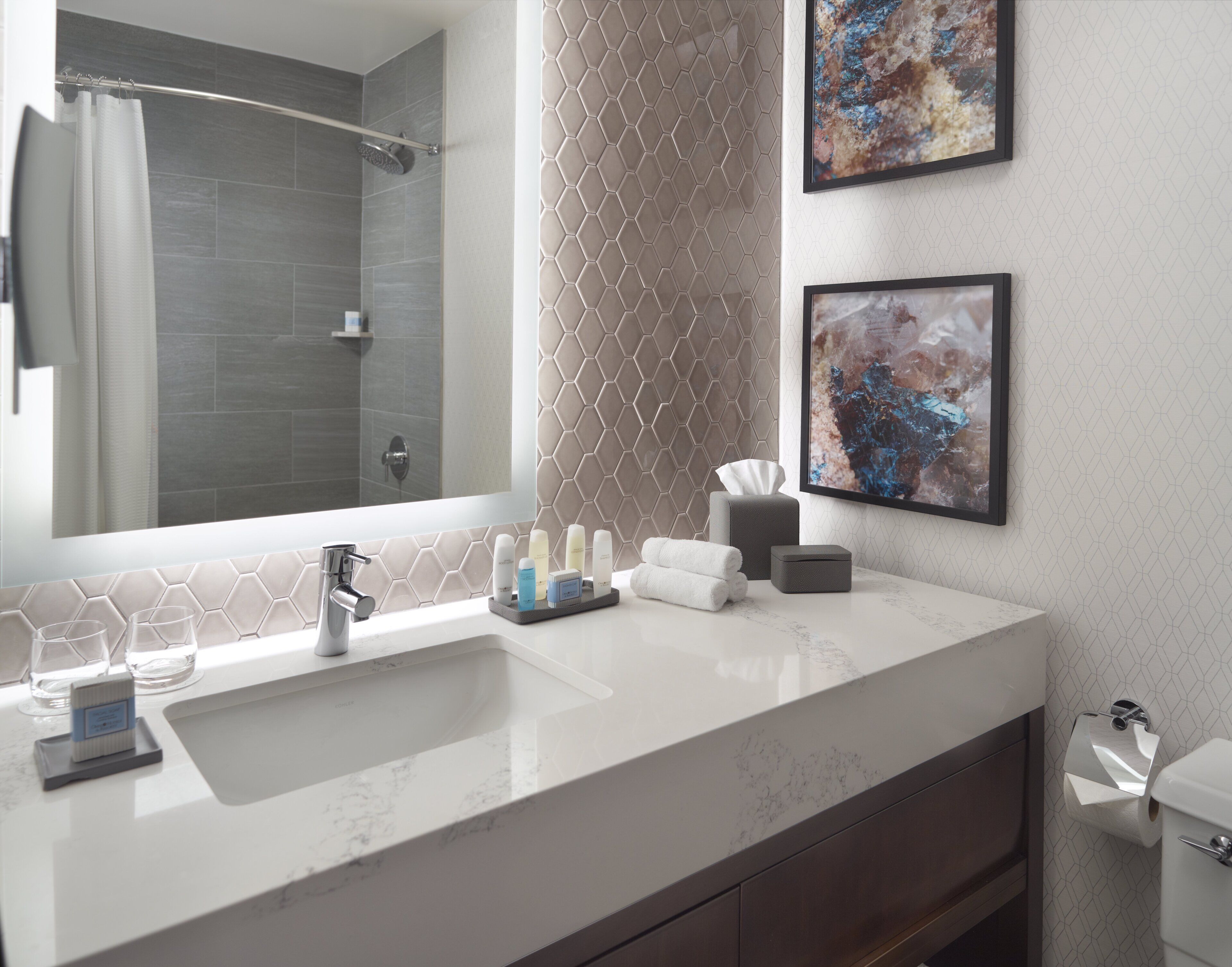 A modern bathroom with a large mirror, a sink, and two framed abstract paintings.