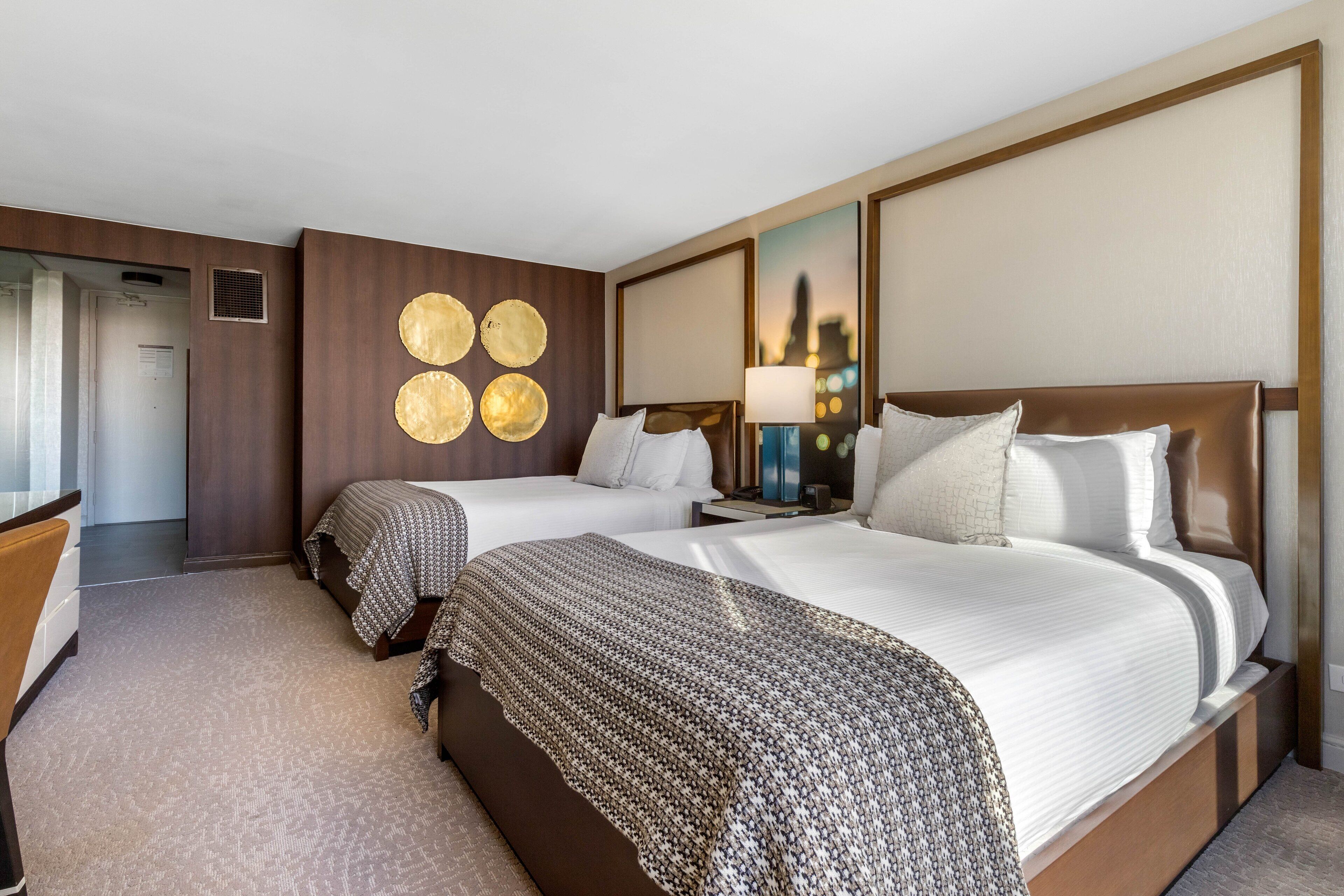 Ein Hotelzimmer mit zwei Betten, einem Schreibtisch und einem Spiegel.