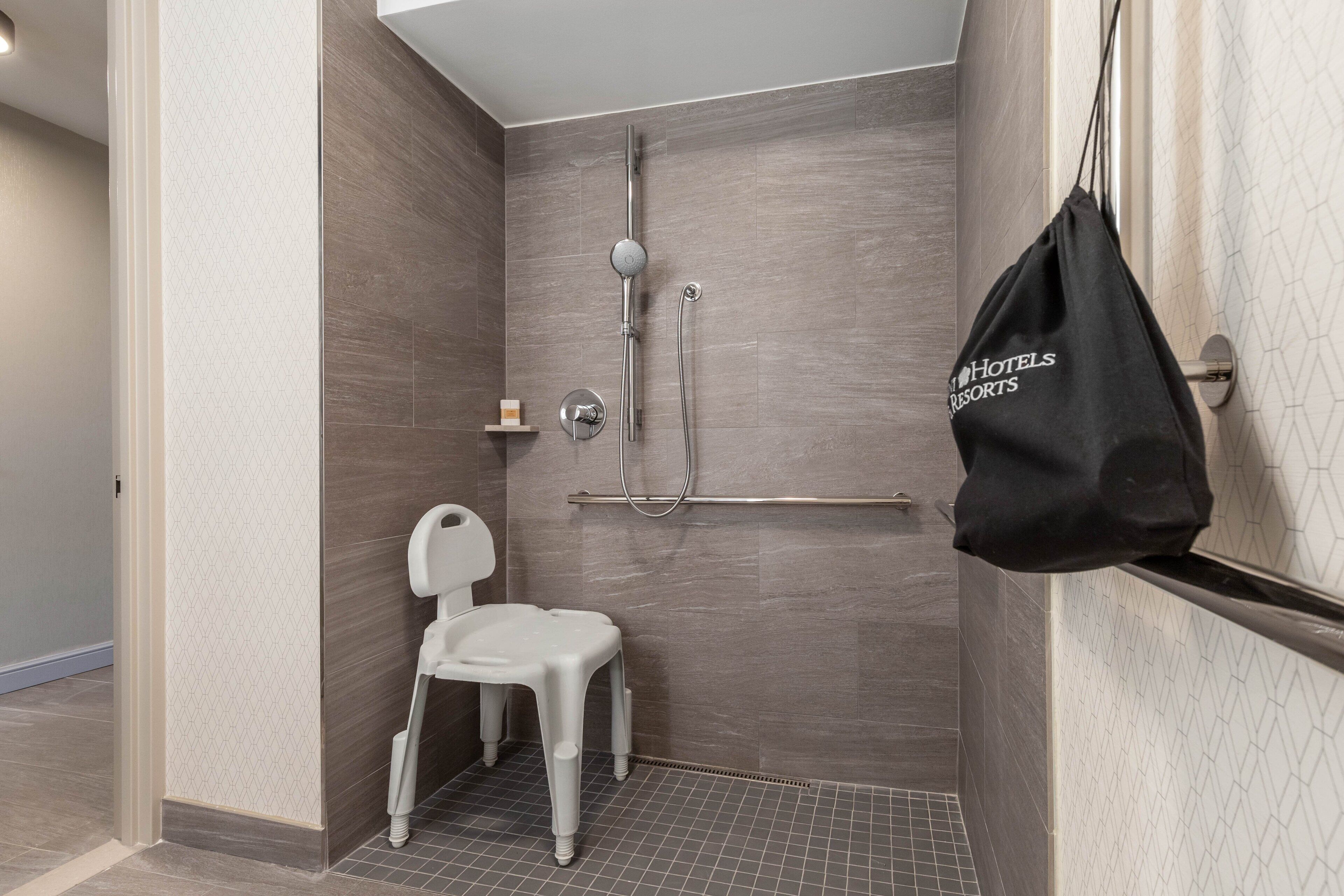 Un baño moderno con ducha, inodoro y una pequeña silla blanca.