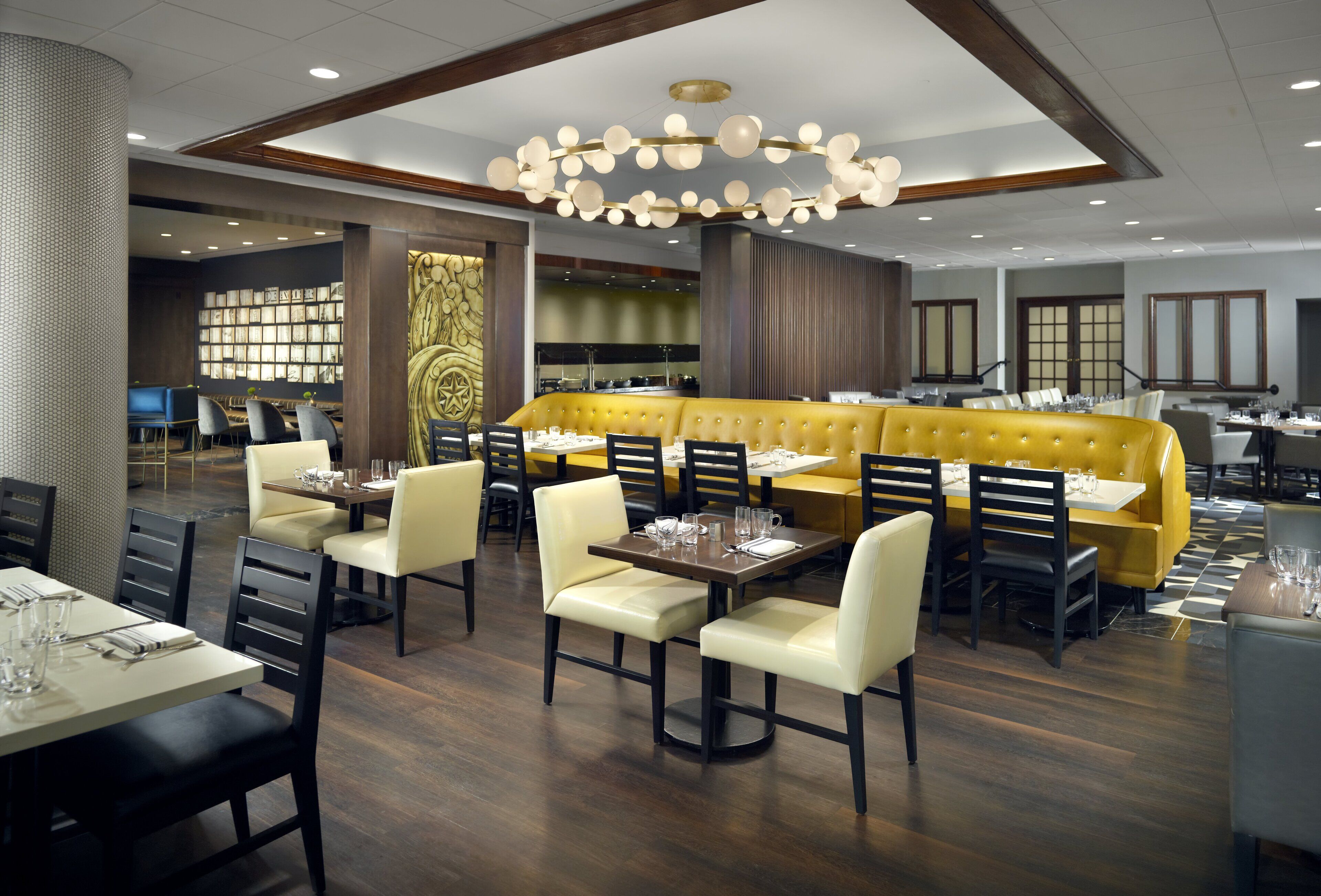 A modern restaurant with a yellow booth seating area, wooden flooring, and a central chandelier.