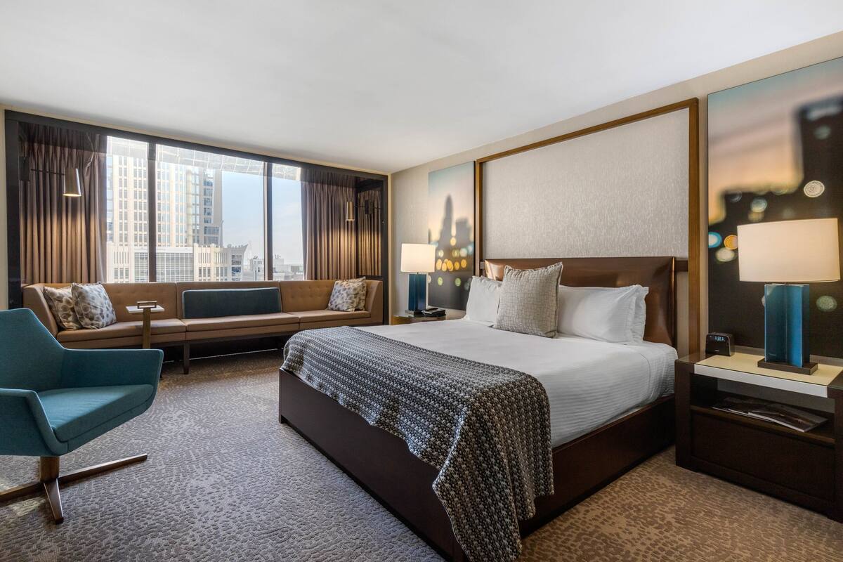 A hotel room with a large bed, a sofa, a desk, and a view of the cityscape.