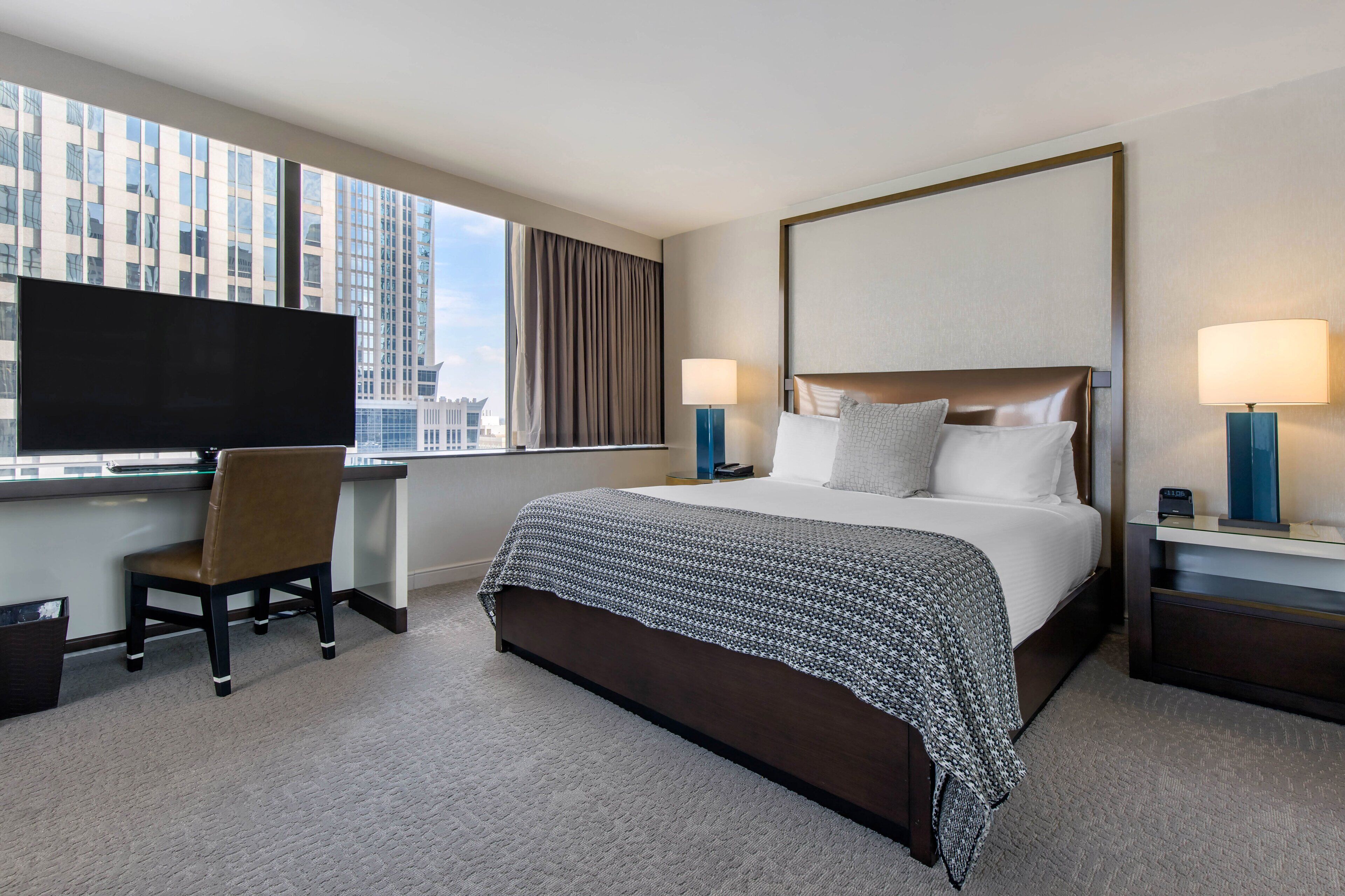 A hotel room with a large bed, a desk with a chair, a TV, and two bedside lamps.