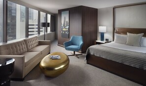 A hotel room with a large bed, a sofa, a blue armchair, a gold ottoman, and a nightstand with a lamp. - Omni Charlotte Hotel (Charlotte)