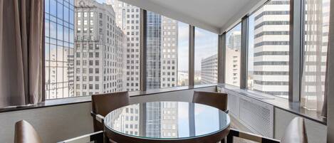 A hotel room with a round glass table and leather chairs, large windows with a city view, and a modern interior design.