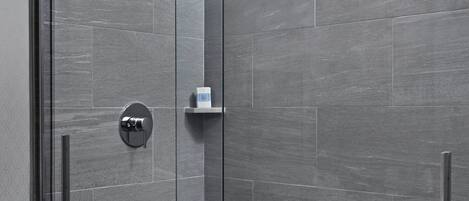 A modern shower with a glass door, a handheld showerhead, and a control panel.