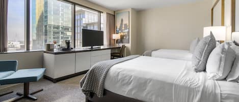 A hotel room with a large bed, a desk with a flat-screen TV, a chair, and a view of a cityscape through large windows.