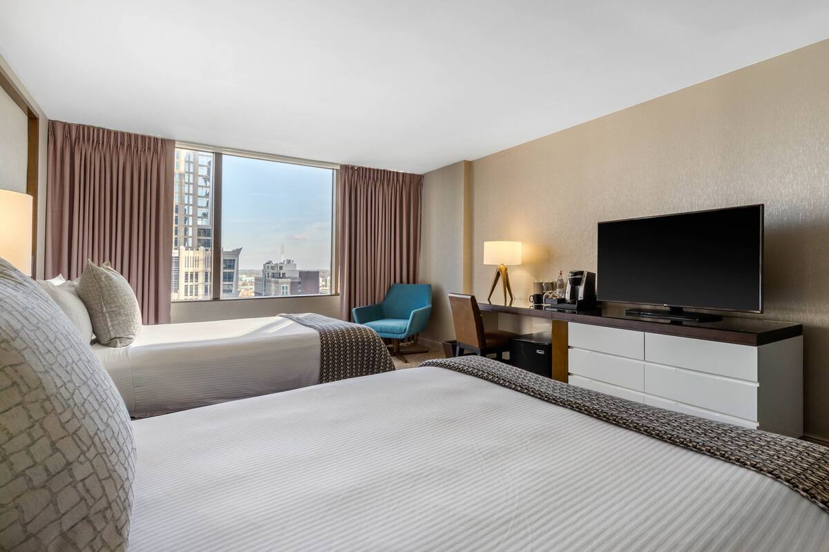 A hotel room with two beds, a TV, a desk with a lamp, and a chair.