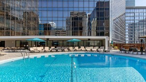A swimming pool with lounge chairs and umbrellas, surrounded by modern buildings.