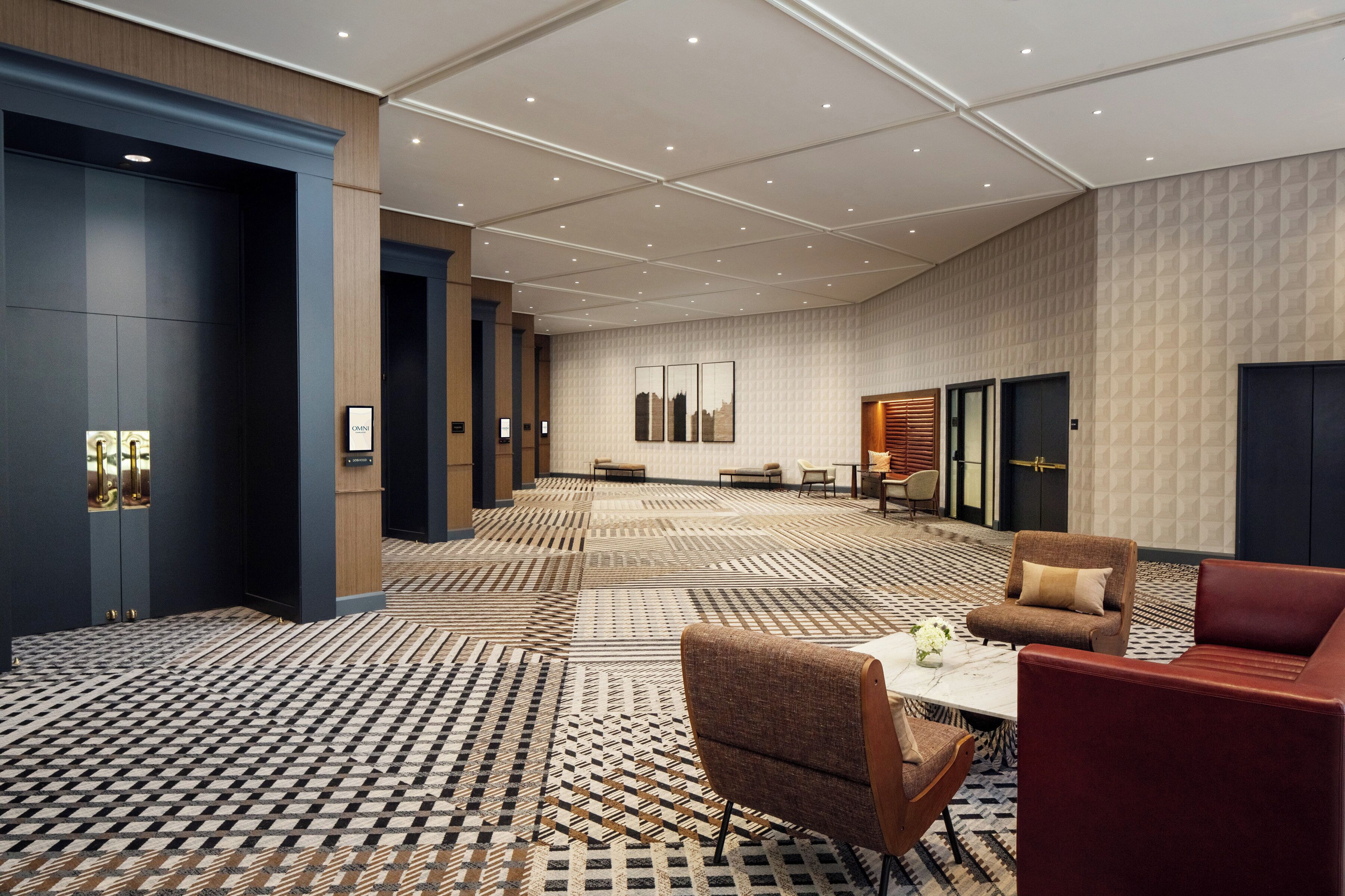A spacious hotel lobby with a patterned carpet, seating area, and modern decor.