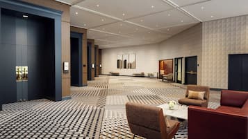 A spacious hotel lobby with a patterned carpet, seating area, and modern decor.