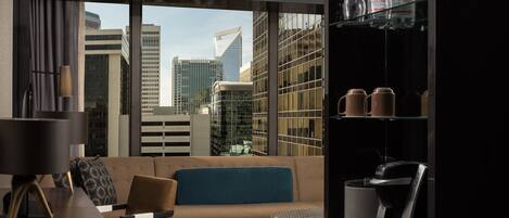 Una habitación de hotel moderna con sofá, cafetera y estante de vidrio con botellas.