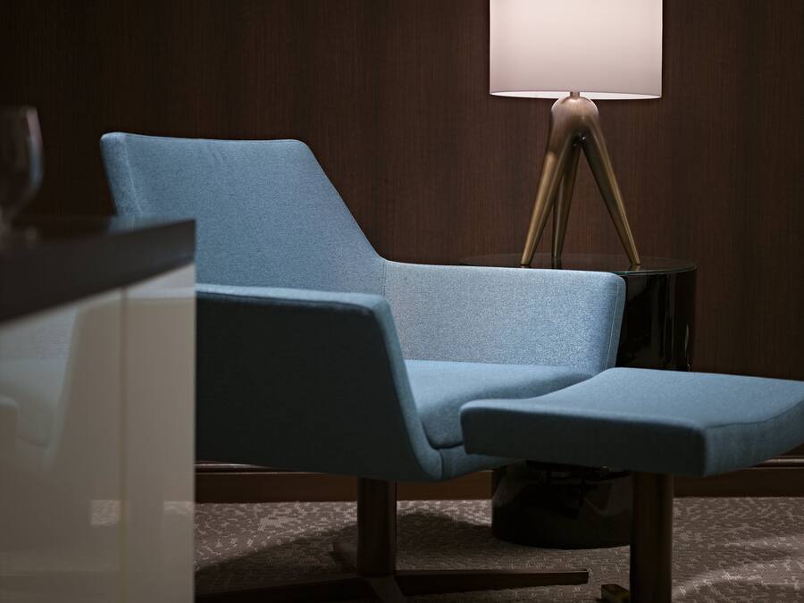 Quarto moderno com uma poltrona azul estofada, um abajur e uma parede de madeira escura.