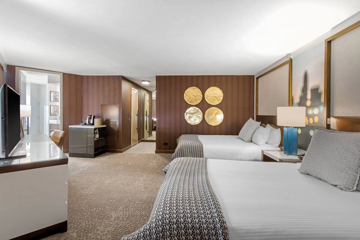 A hotel room with a large bed, a smaller bed, a desk, a TV, and a wardrobe. There are wall-mounted circular decorations and a lamp on the bedside table.