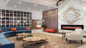 A modern lobby with a blue sofa, a round coffee table, a fireplace, and a large window with a view of the city. - Delta Hotels by Marriott Indianapolis Airport (Indianapolis)