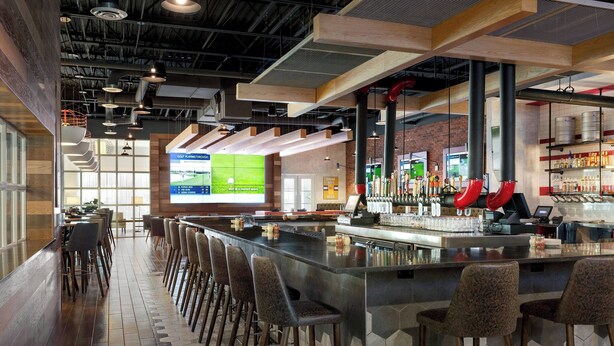 A bar area with a long counter, multiple stools, and a large screen displaying sports content. - Delta Hotels by Marriott Indianapolis Airport (Indianapolis)
