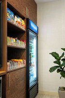 Una habitación de hotel con un mueble de madera repleto de aperitivos y un refrigerador minibar.