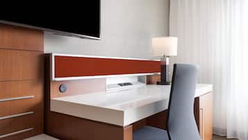 Une chambre d’hôtel équipée d’un bureau en bois, d’un téléviseur à écran plat, d’une lampe et d’une chaise.
