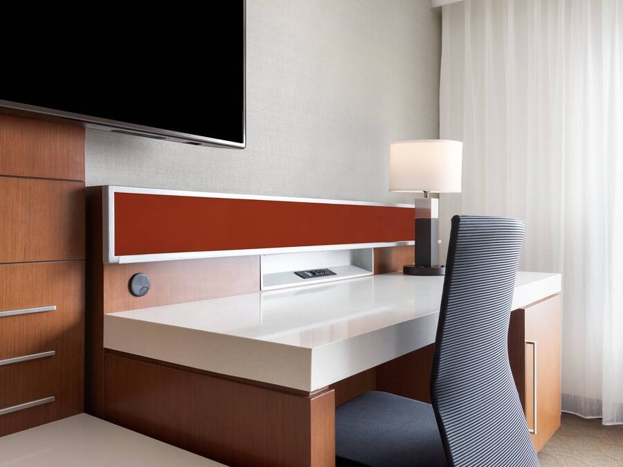 Une chambre d’hôtel équipée d’un bureau en bois, d’un téléviseur à écran plat, d’une lampe et d’une chaise.