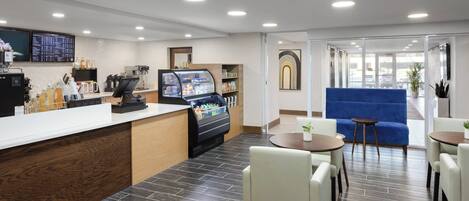 A modern hotel lobby with a reception desk, coffee machines, a self-service beverage station, seating area, and a blue sofa.
