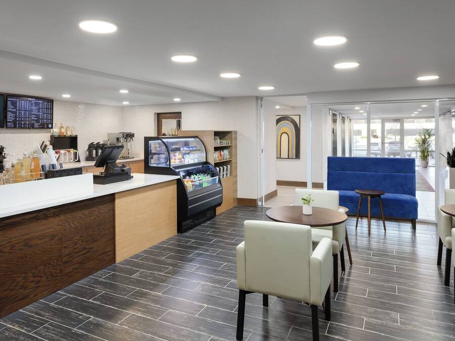 A modern hotel lobby with a reception desk, coffee machines, a self-service beverage station, seating area, and a blue sofa.