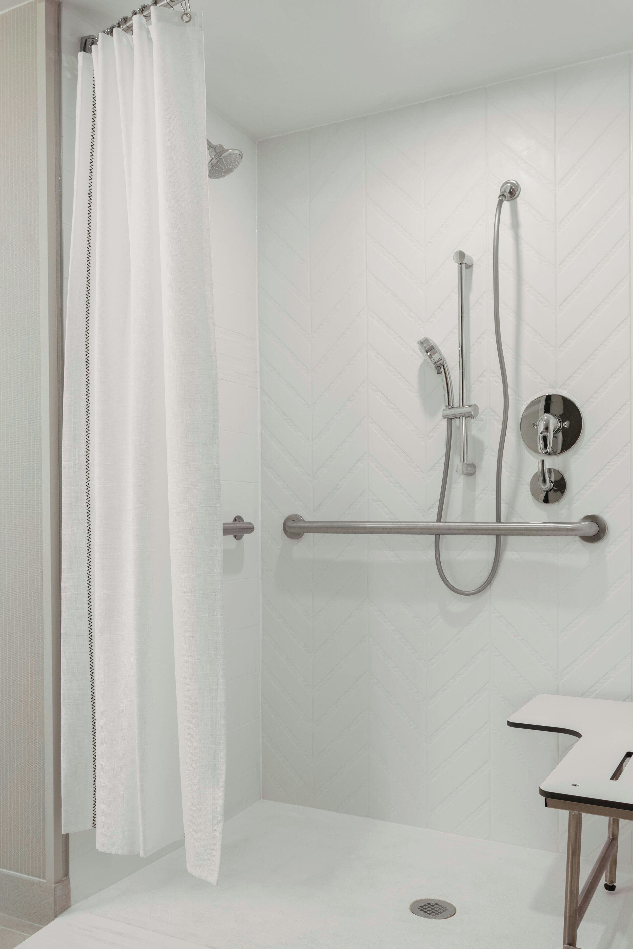 Un área de ducha moderna con cortina blanca, cabezal de ducha manual y grifo empotrado en la pared.