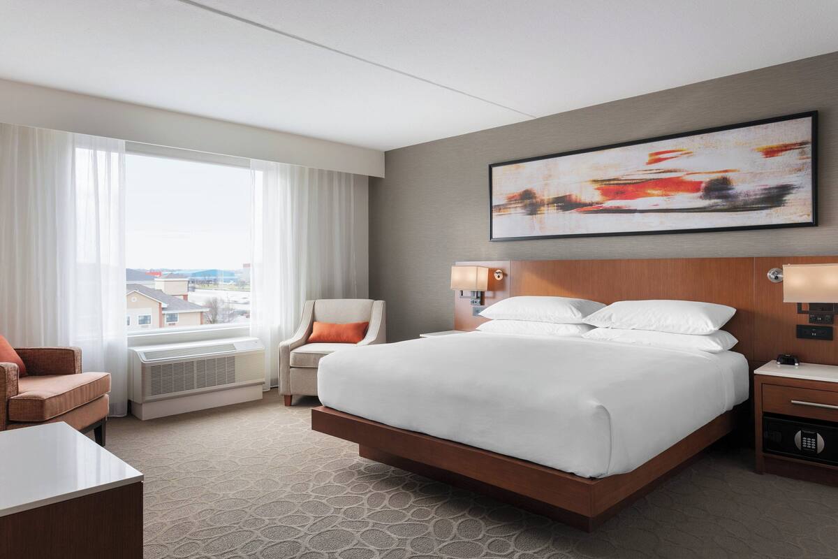 Une chambre d’hôtel avec un grand lit, une chaise, un bureau et une fenêtre avec des rideaux.