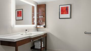 Un baño moderno con un lavamanos blanco, tocador de madera y estantes con artículos de aseo.