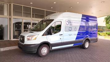 A white and blue Delta Hotels van parked in front of a building with large windows.