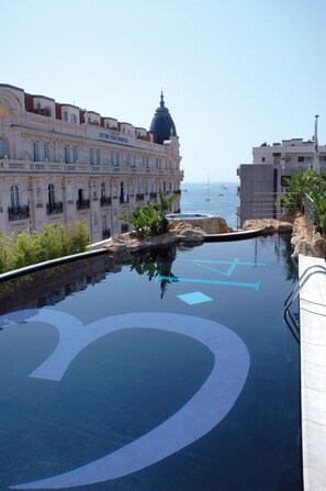 A pool with a large circular design, surrounded by buildings with balconies and a view of the sea. - 3.14 Hotel (Cannes)