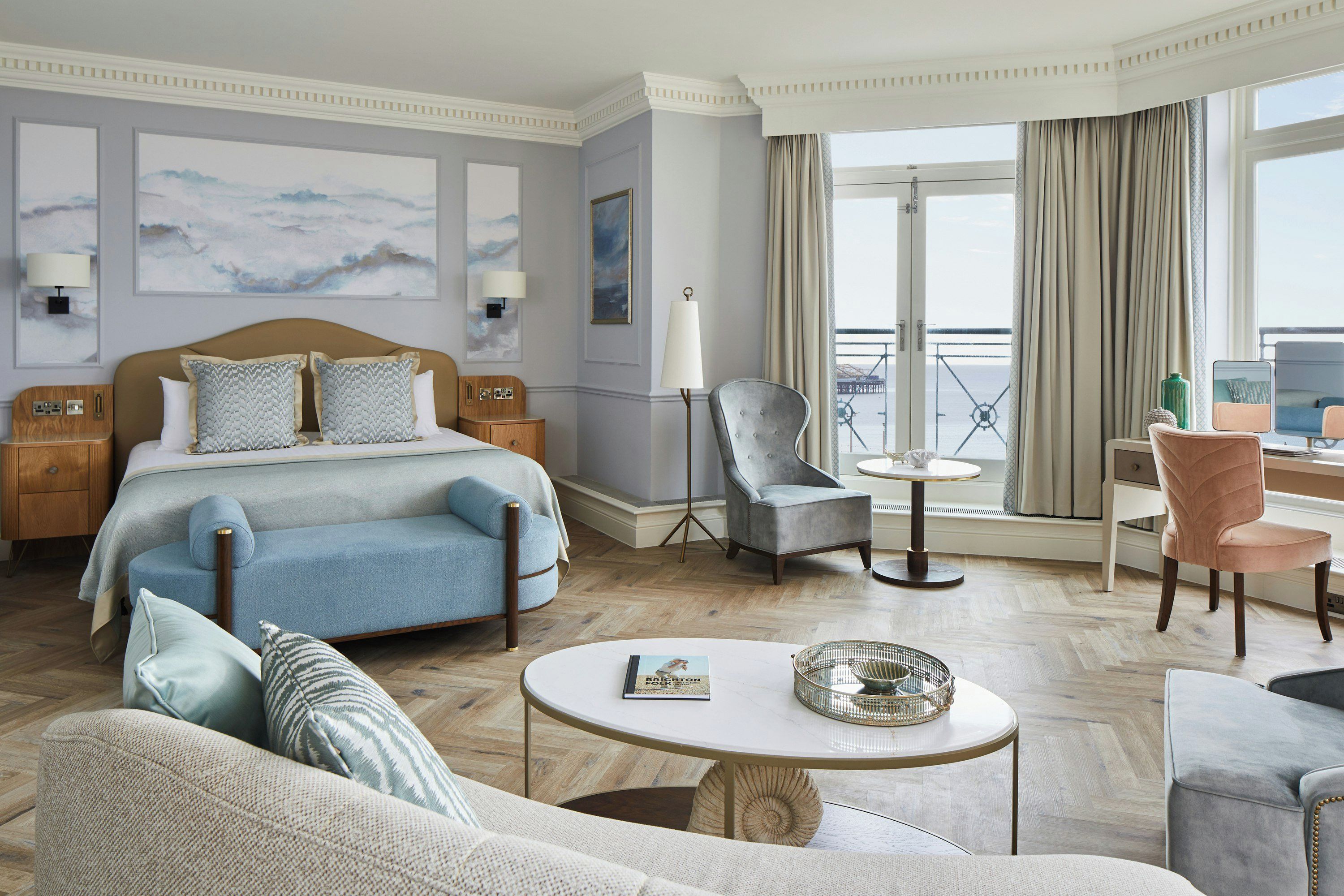 Habitación de hotel con una cama, dos sillones, un sofá, una mesita redonda, un escritorio y un balcón con vistas.
