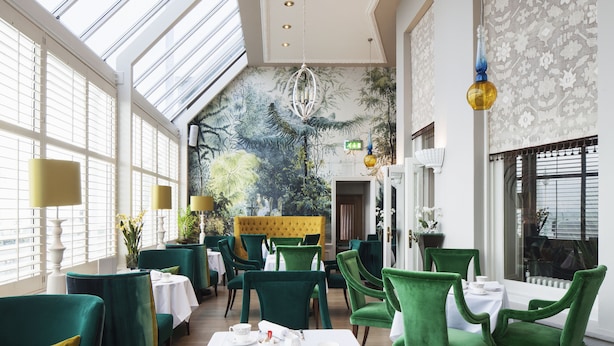 A restaurant with green upholstered chairs and tables, a large mural on the wall, and a high ceiling with skylights. - The Grand Brighton (Brighton)