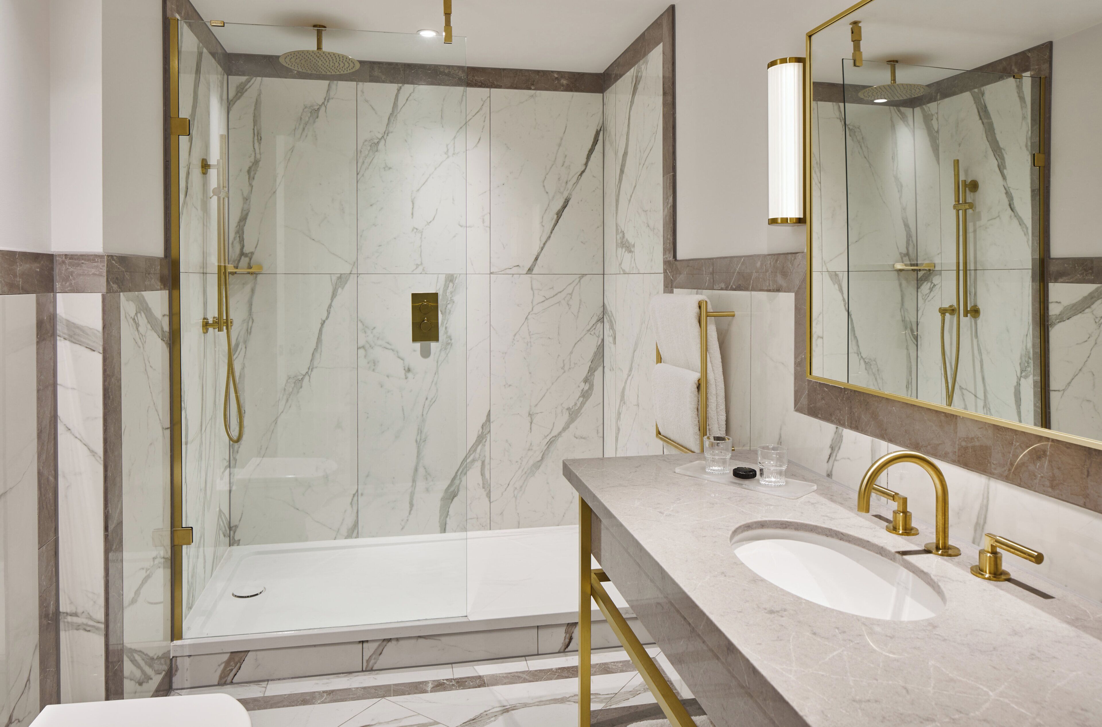 Un baño moderno con ducha envuelta en vidrio, tocador con lavamanos y un espejo grande.
