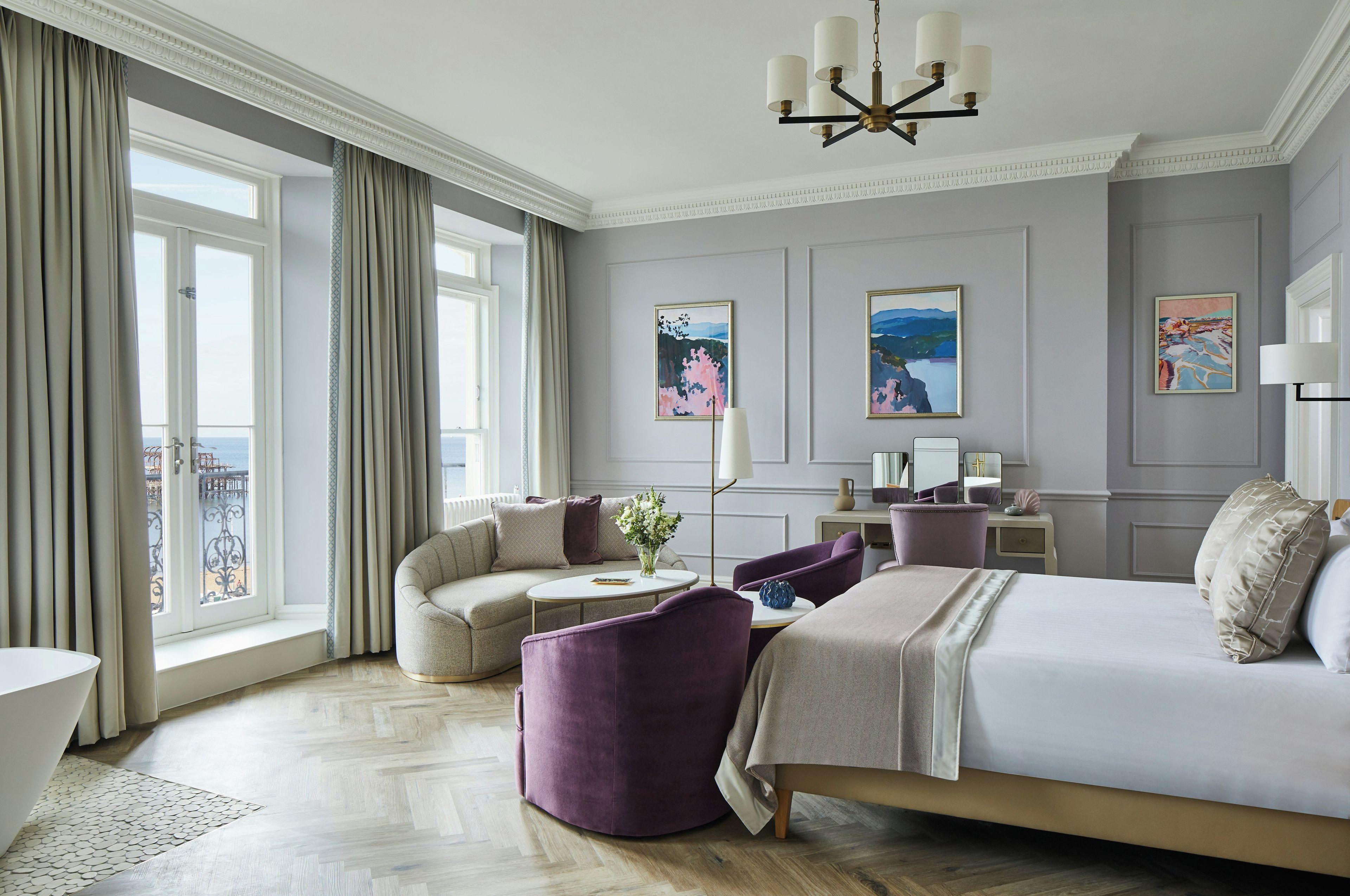 A hotel room with a large bed, a seating area with a sofa and armchairs, a small table, and artwork on the walls.