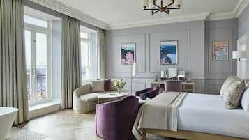 A hotel room with a large bed, a seating area with a sofa and armchairs, a small table, and artwork on the walls.