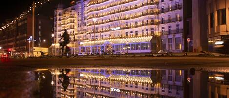 Un hotel de varios pisos con balcones y su reflejo en el agua.