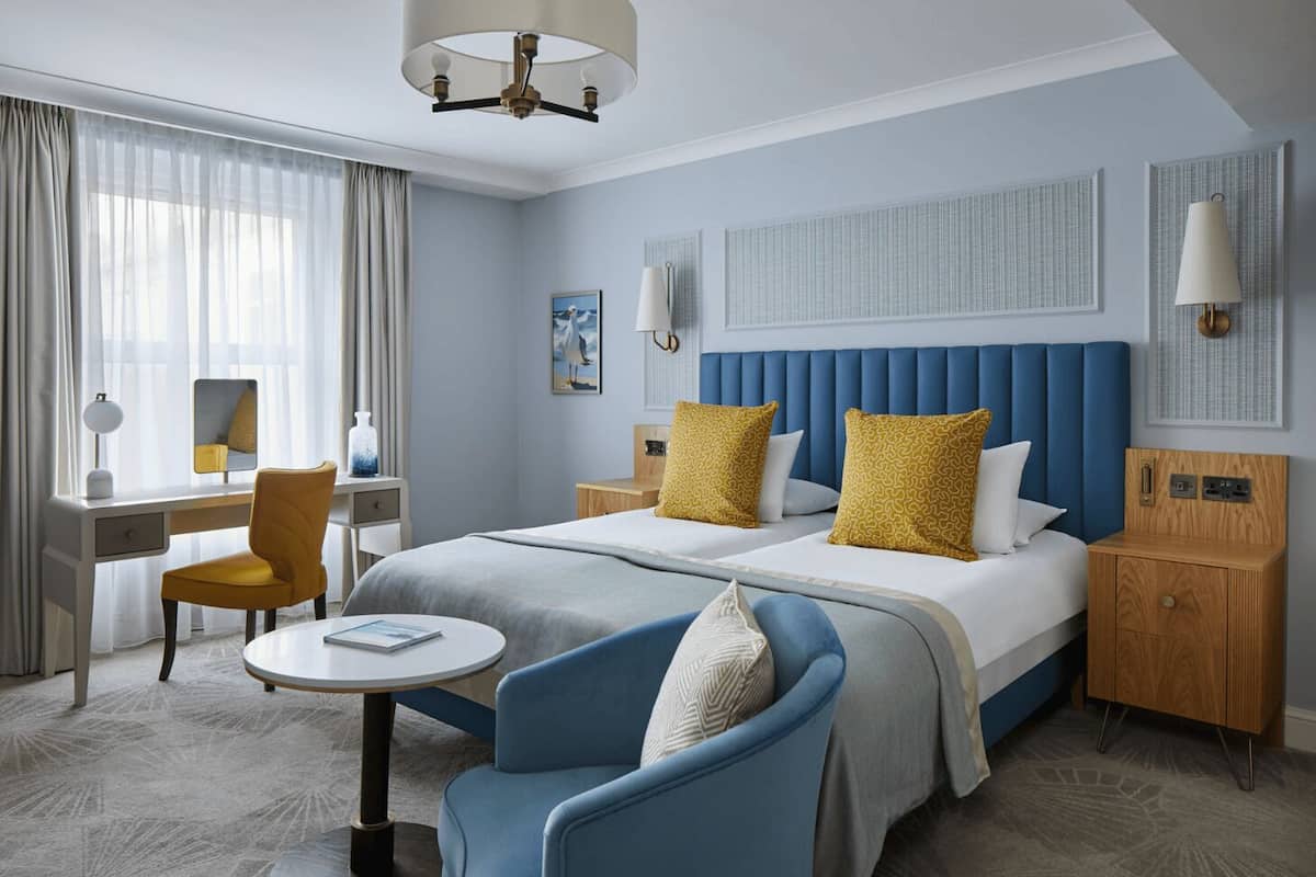 Une chambre d’hôtel avec un grand lit, un bureau, une chaise, une petite table et une table de chevet.