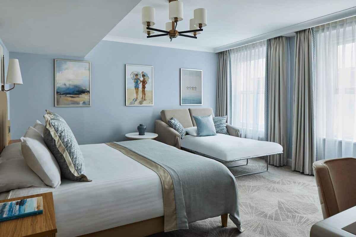 Une chambre d’hôtel avec deux lits, un canapé, une petite table et un lustre.