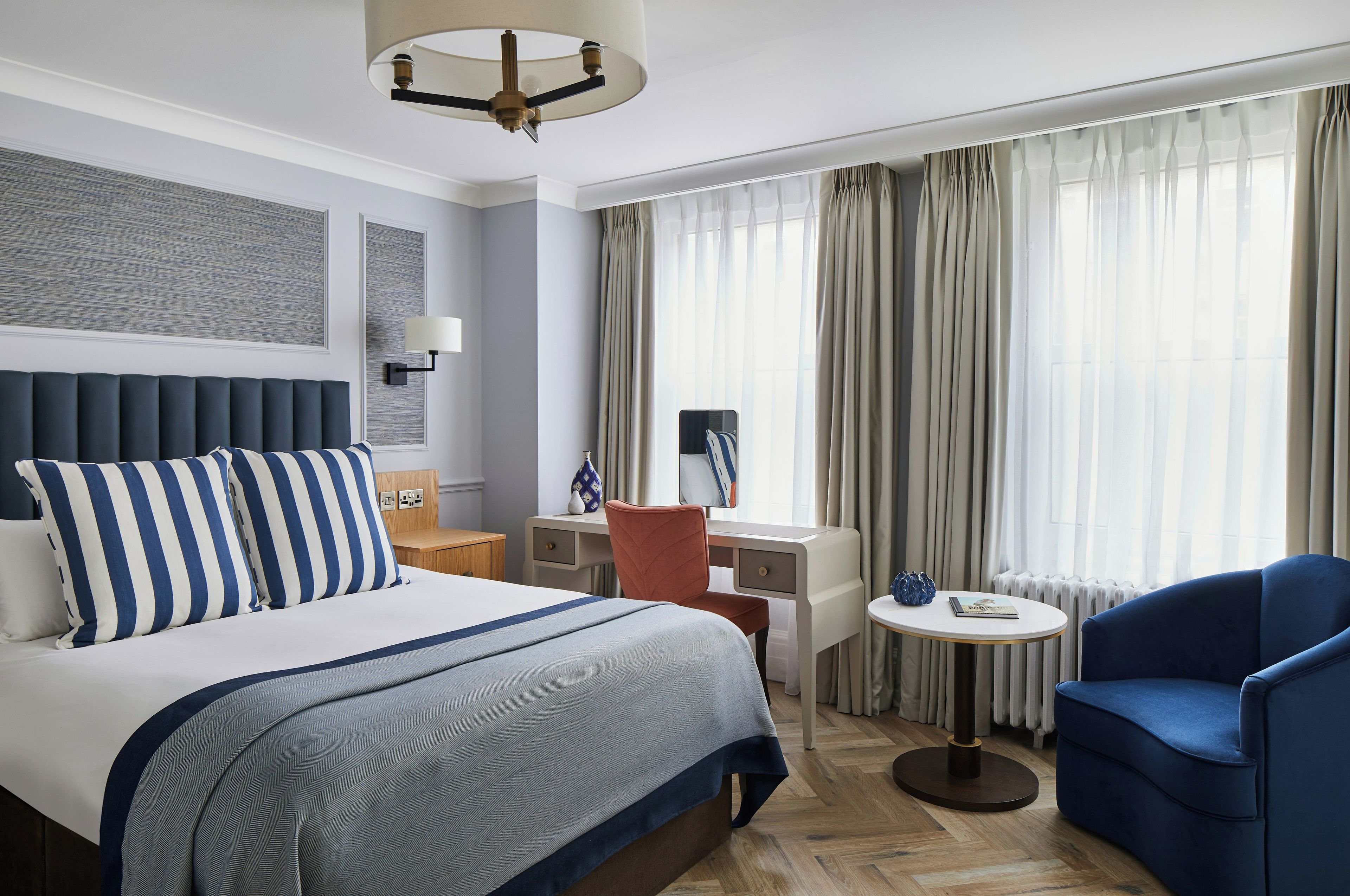 A hotel room with a bed, a desk, a chair, a round table, and a large window with curtains.