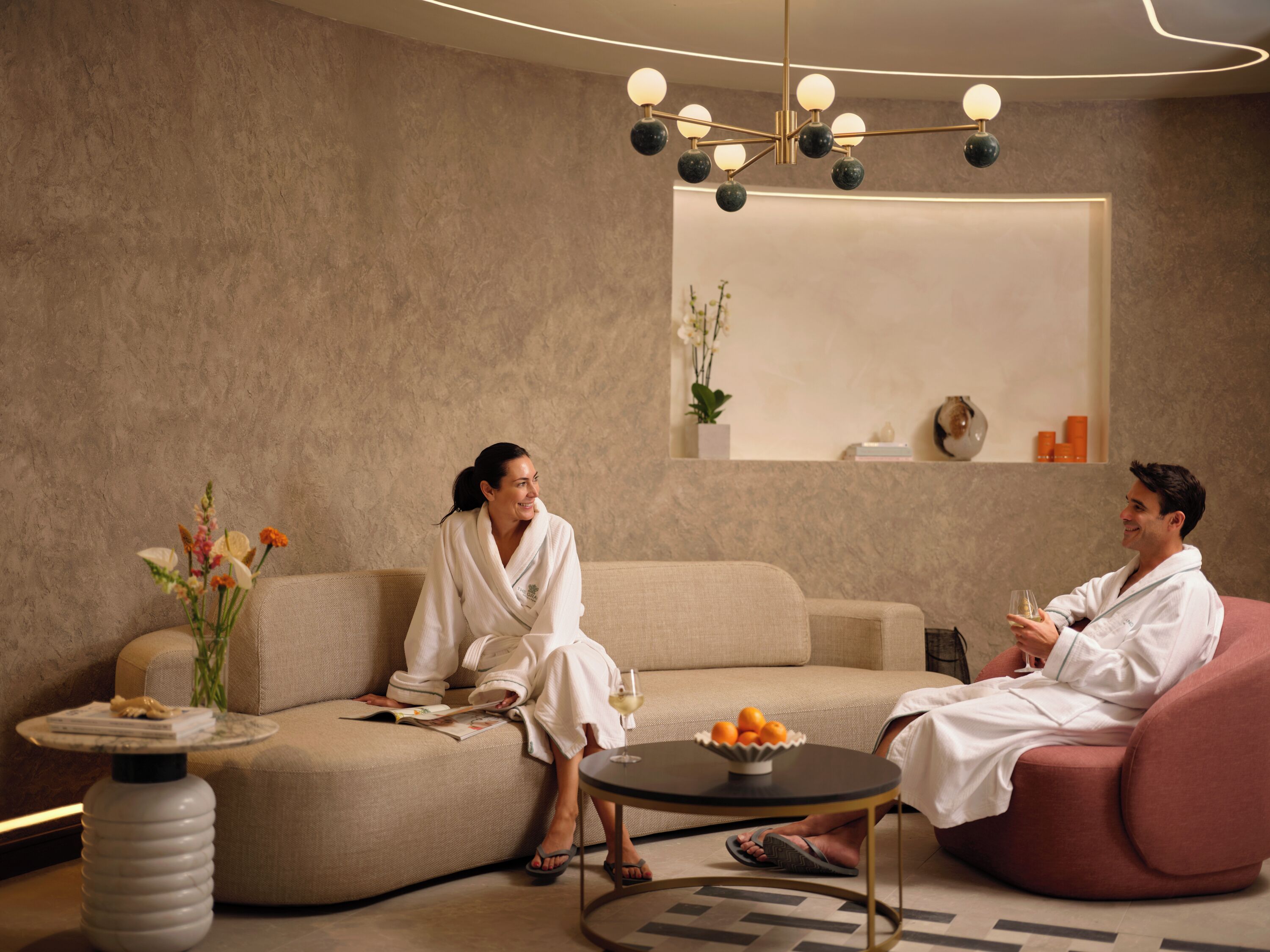 A modern spa room with a sofa, a round table with fruit, and a unique chandelier.