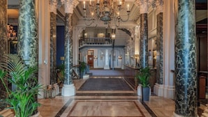 A grand lobby with marble columns, a chandelier, and a staircase leading to an upper level. - The Grand Brighton (Brighton)