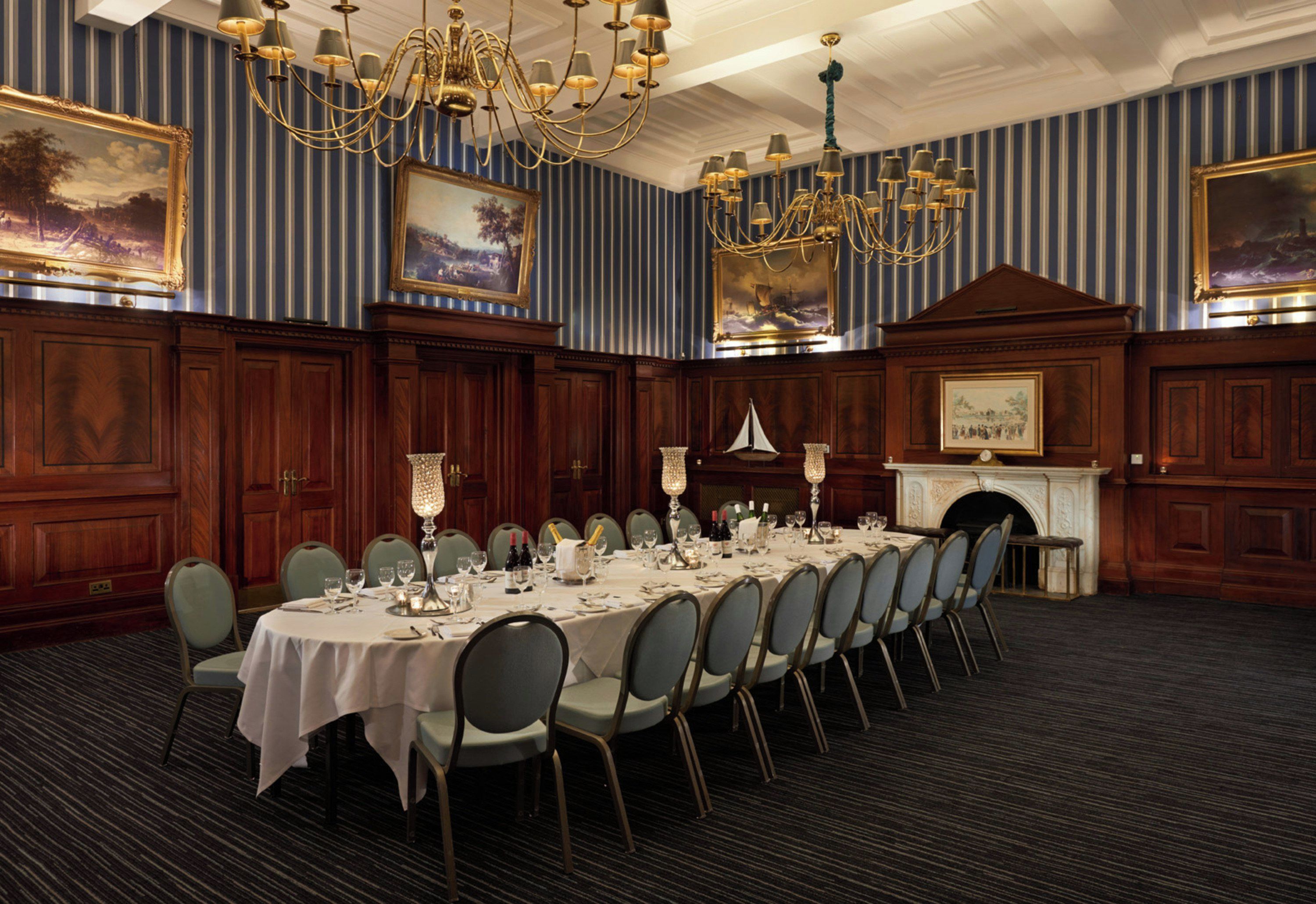 Comedor formal con una larga mesa dispuesta para un banquete, flanqueada por paneles de madera y cuadros enmarcados.