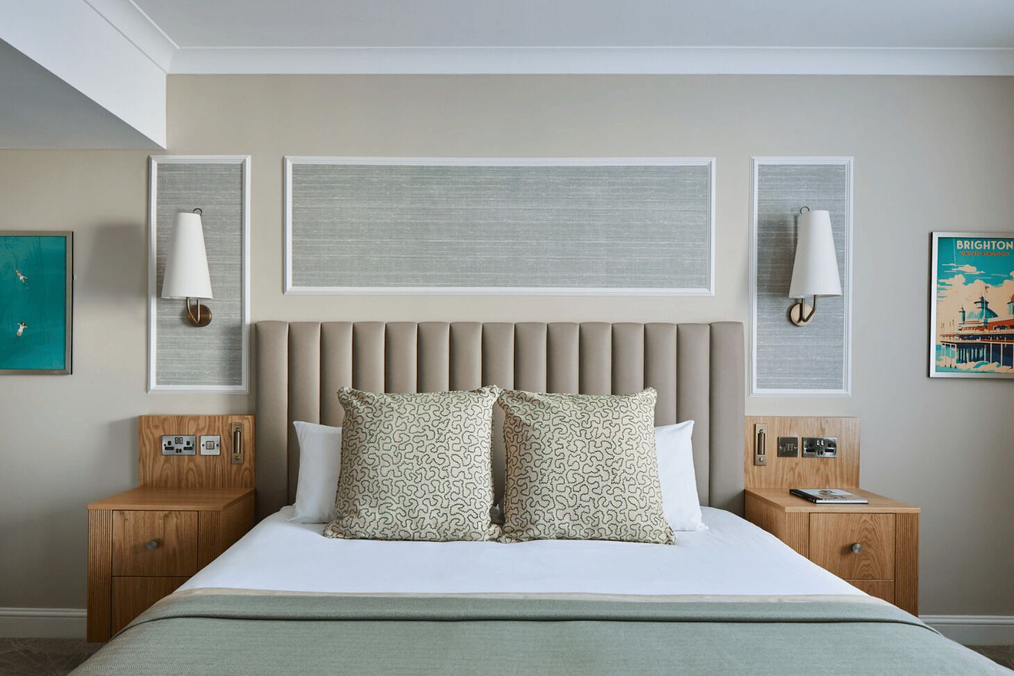 A hotel room with a large bed, two bedside tables, a headboard, and wall-mounted lamps.