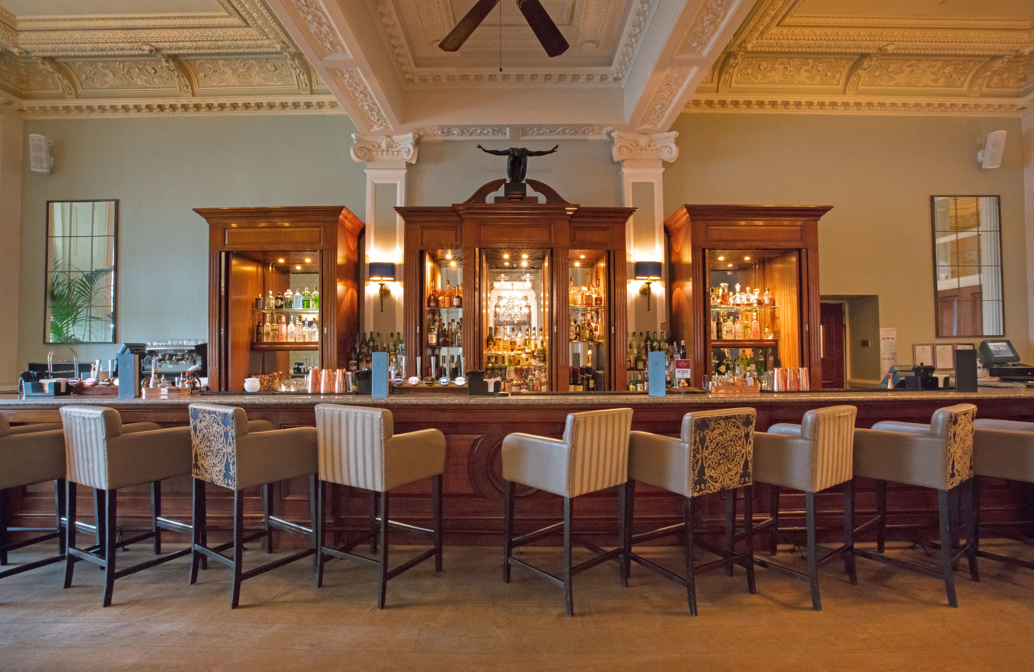 A bar area with a central bar counter, multiple bar stools, and a decorative ceiling fan.
