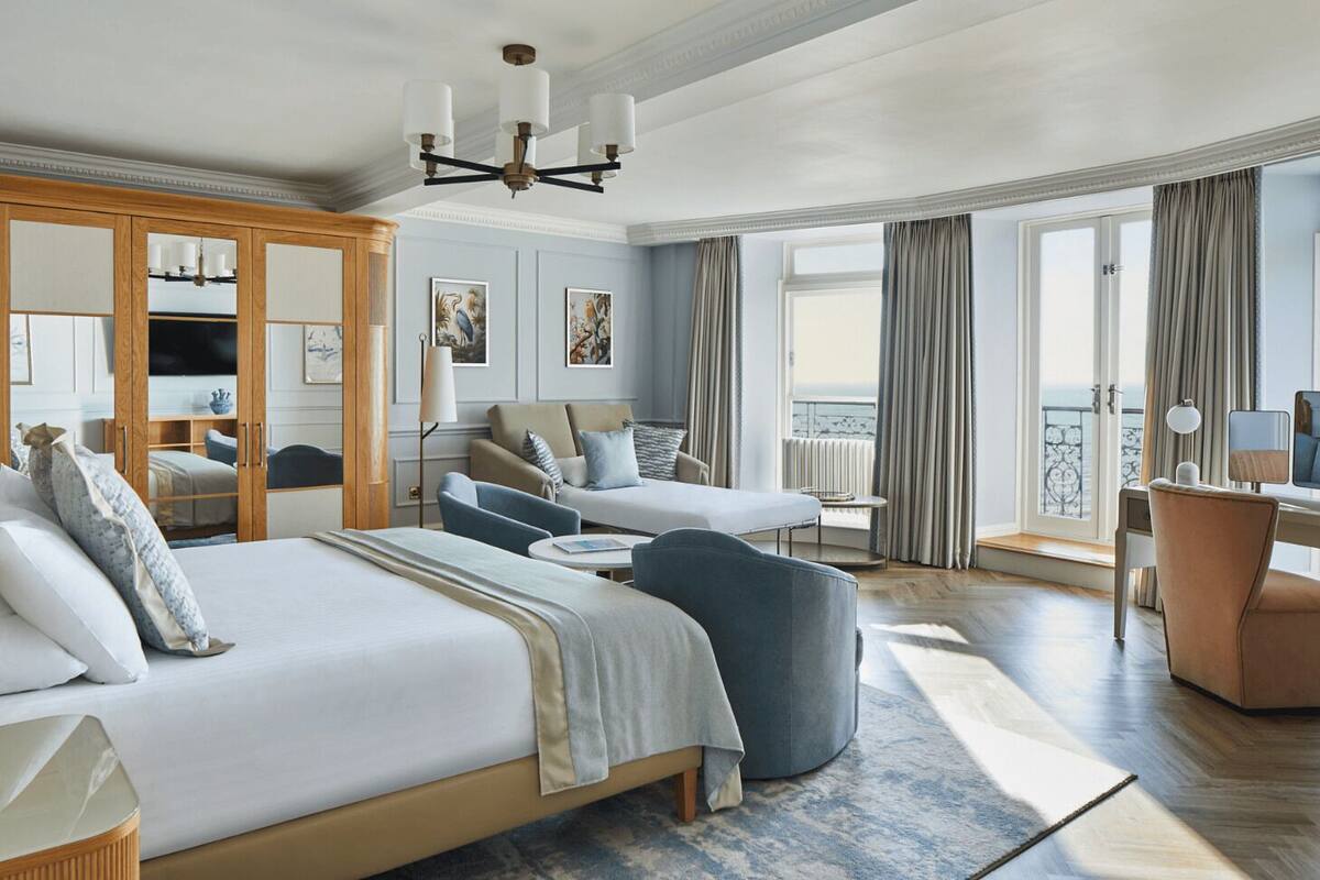 Une chambre d’hôtel avec un grand lit, deux fauteuils, un bureau et un balcon avec des rideaux.
