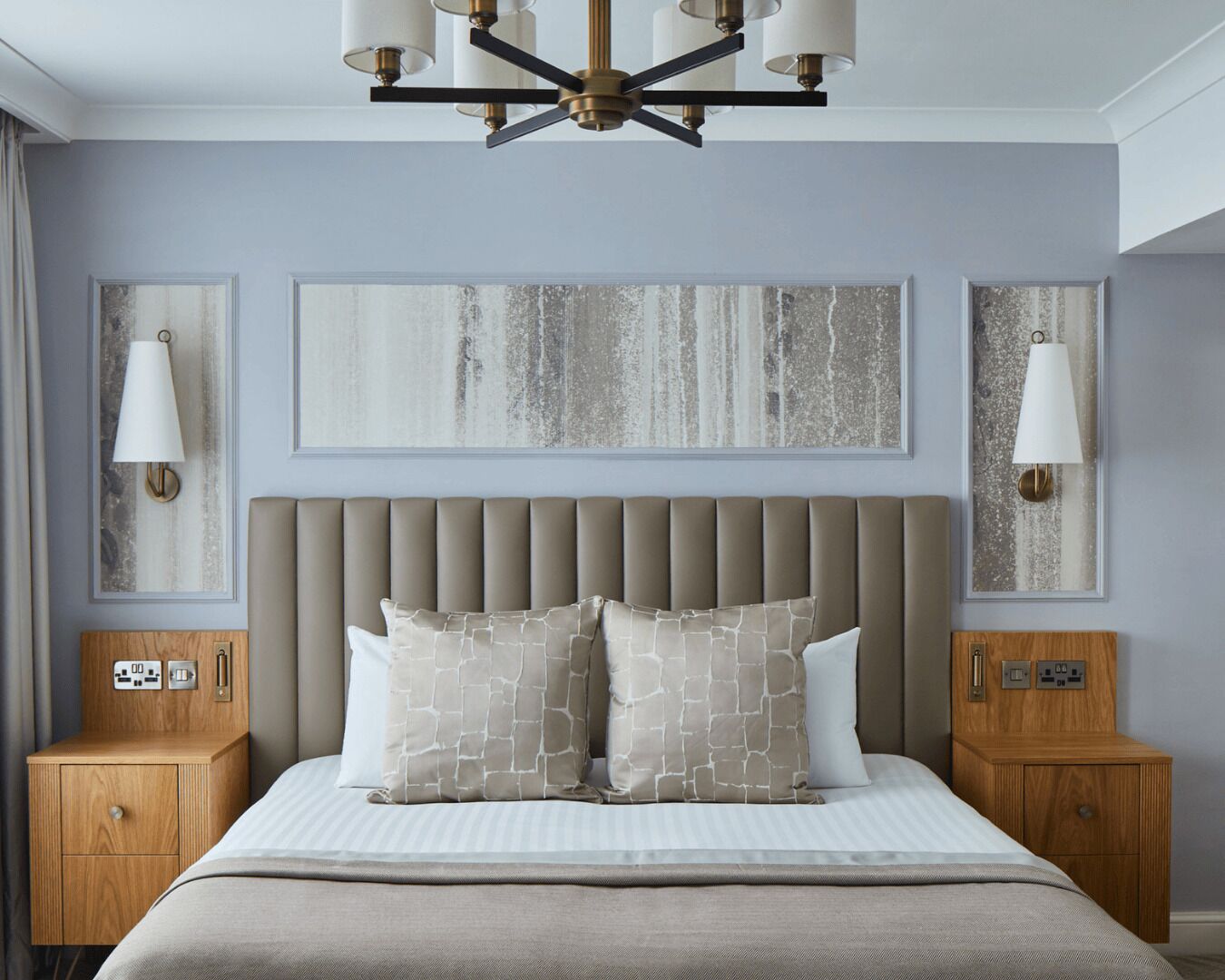 A bedroom with a tufted headboard, two bedside tables, a chandelier, and abstract wall art.