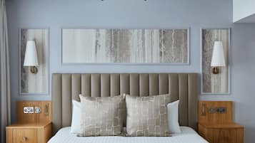 A bedroom with a tufted headboard, two bedside tables, a chandelier, and abstract wall art.