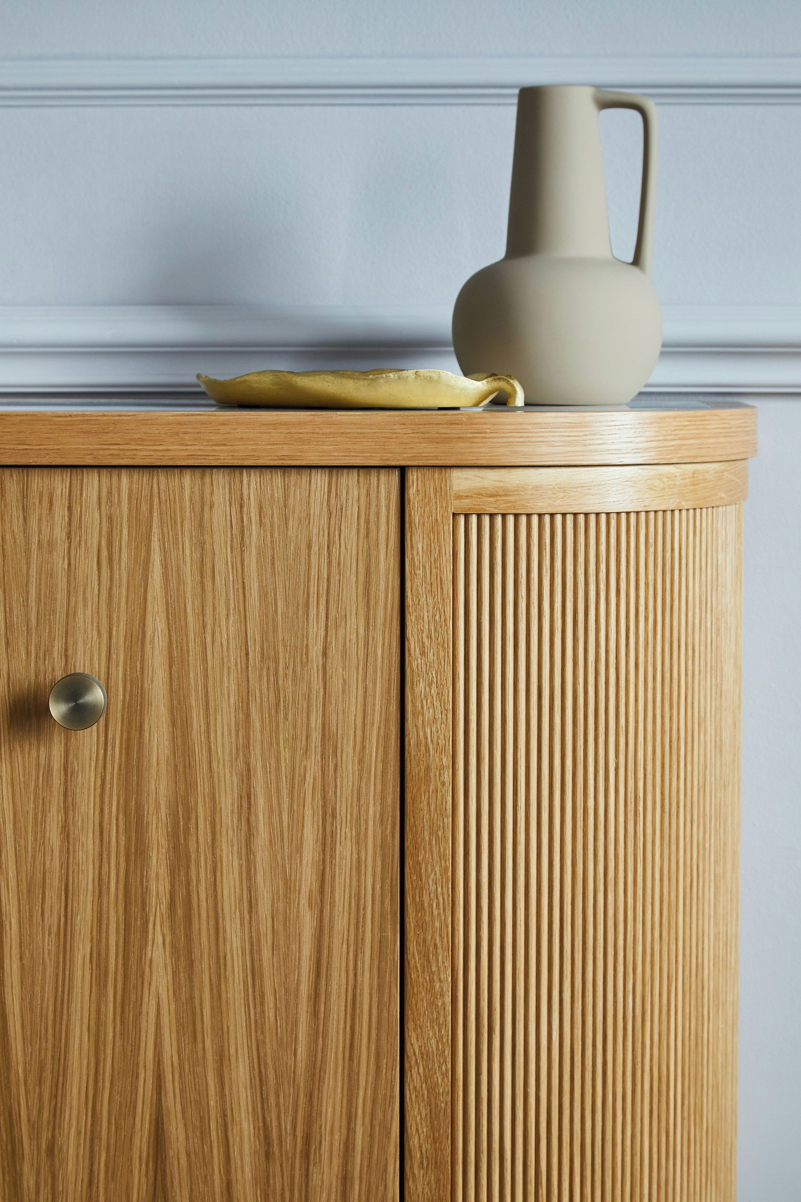 A wooden cabinet with a single door and a handle, a beige pitcher, and a yellow plate on top.